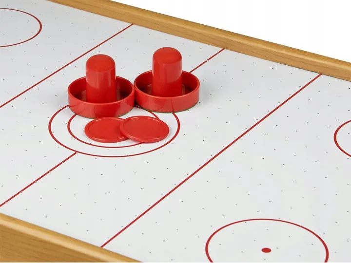 Air Hockey spēles laukuma tuvplāns ar diviem sarkaniem sitējiem un ripām