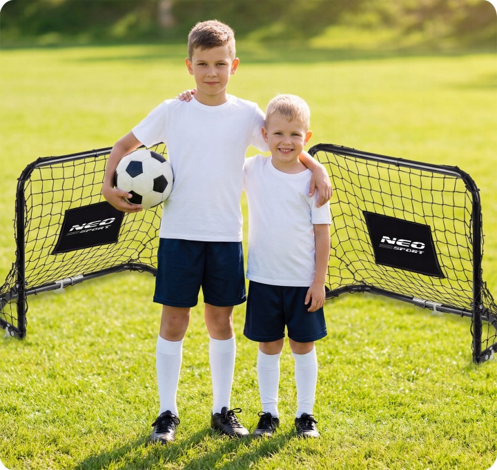 Divi bērni pie futbola vārtiem ārā uz zaļa zāliena