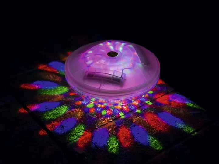 LED peldlampa uz tumša fona ar daudzkrāsainu gaismas vainagu zem lampas