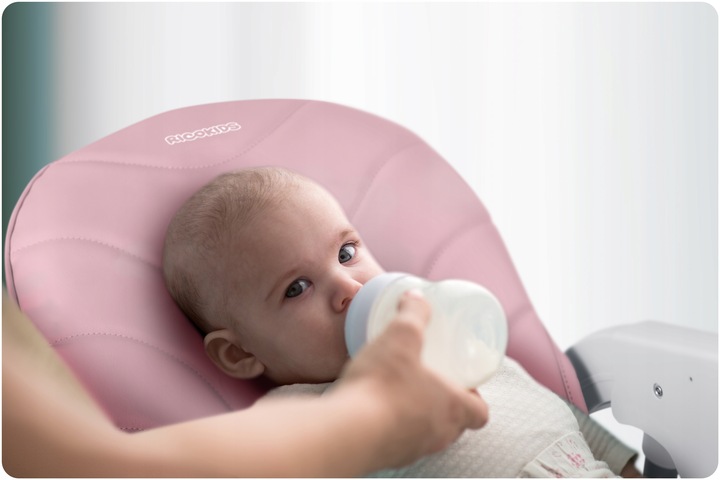 Bērns pusguļus pozīcijā rozā Ricokids Tulo barošanas krēslā ar pudelīti