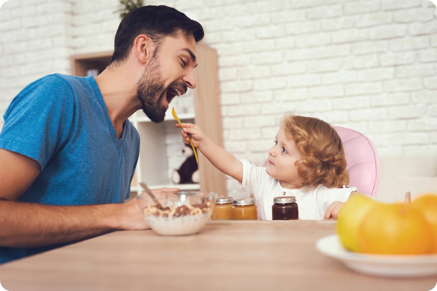 Bērns tiek barots pie galda, fonā redzams rozā Ricokids Tulo barošanas krēsls