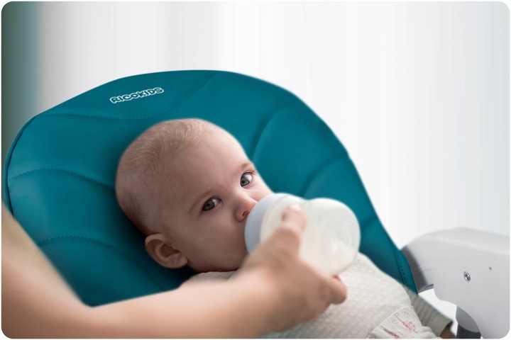 Mazulis Ricokids Tulo barošanas krēslā, kuram tiek dots pudeļu ēdiens, redzams mīksts galvas balsts
