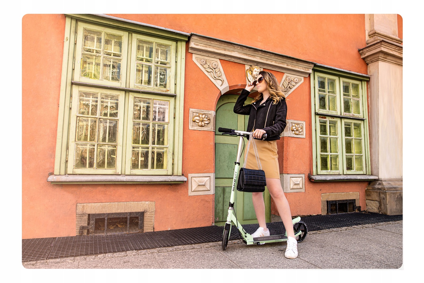 SOKE City Green skrejritenis pie oranžas fasādes, lietotāja poza pilsētvidē