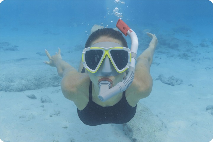 Snorkelētāja zem ūdens ar masku un elpošanas caurulīti, redzama zilgana zemūdens vide