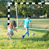 Bērni spēlē futbolu pie lieliem futbola vārtiem saulainā parkā