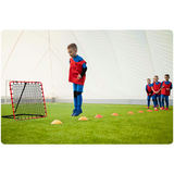 Bērnu futbola treniņa aina ar rebounder iekštelpu laukumā un konusiem