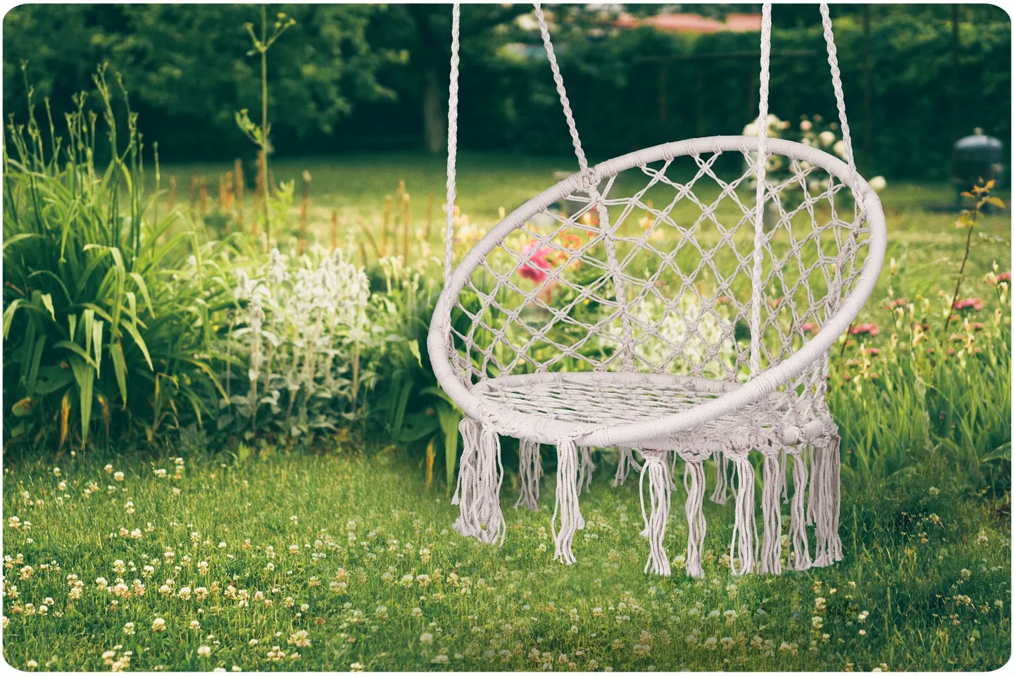 Boho piekaramais krēsls dārzā, redzams sānskats ar pītu pinumu un garām bārkstīm