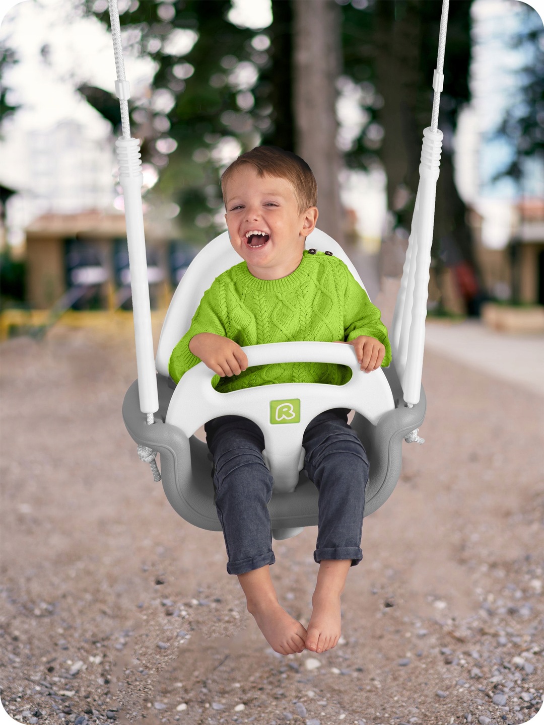 Bērns sēž Ricokids šūpolēs ārā ar redzamām līnijām un drošības stieni
