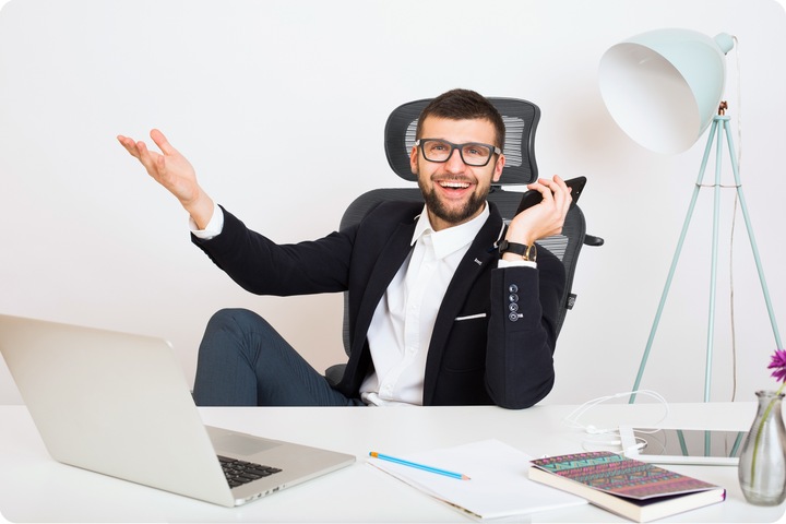 Smaidošs vīrietis sēž ergonomiskā biroja krēslā pie rakstāmgalda