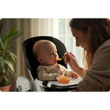 Barošanas mirklis ar bērnu krēsliņā, paplāti un vecāka roku ar karoti