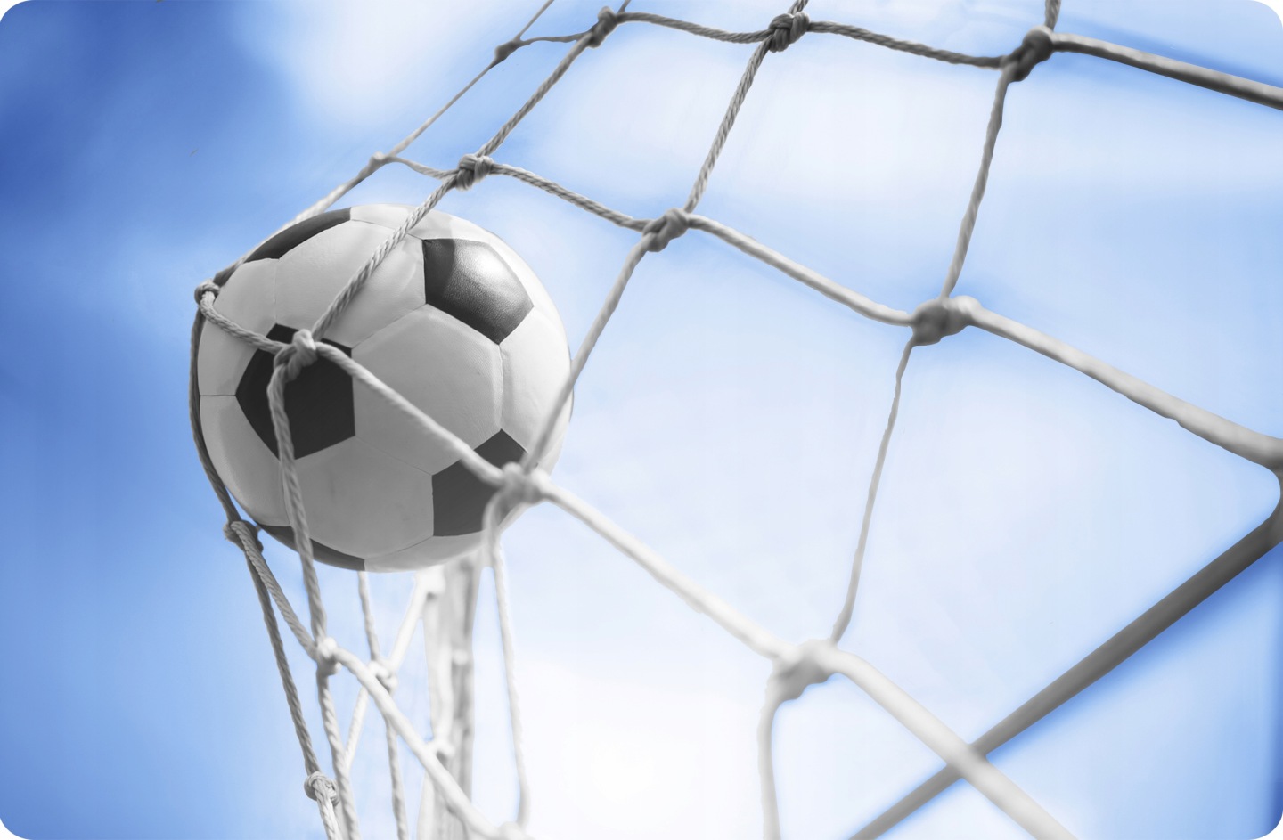 Futbola vārtu tīkla mezgli un bumba iesprostota tīkliņā pret zilām debesīm, tuvplāns